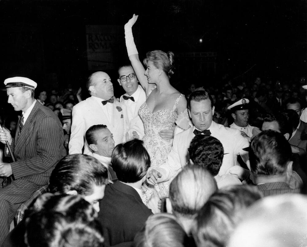 <b> Sofija Loren  </b>  
Jedno od najglamuroznijih venecijanskih izdanja videli smo na italijanskoj glumici Sofiji Loren 1955. godine, kada je čuvena lepotica prošetala u očaravajućoj koktel haljini. Ona se odlučila za krem toaletu s korsetom i širokim bretelama, koju je krasio srcoliki dekolte, a čitava haljina prekrivena je pažljivo prišivenim šljokicama.
Upotpunila ju je elegantnim belim rukavicama i dijamantskim visećim minđušama, dok je kosu podigla i u prvi plan istakla lepotu svog lica. Niko to nije umeo kao Sofija, zar ne?