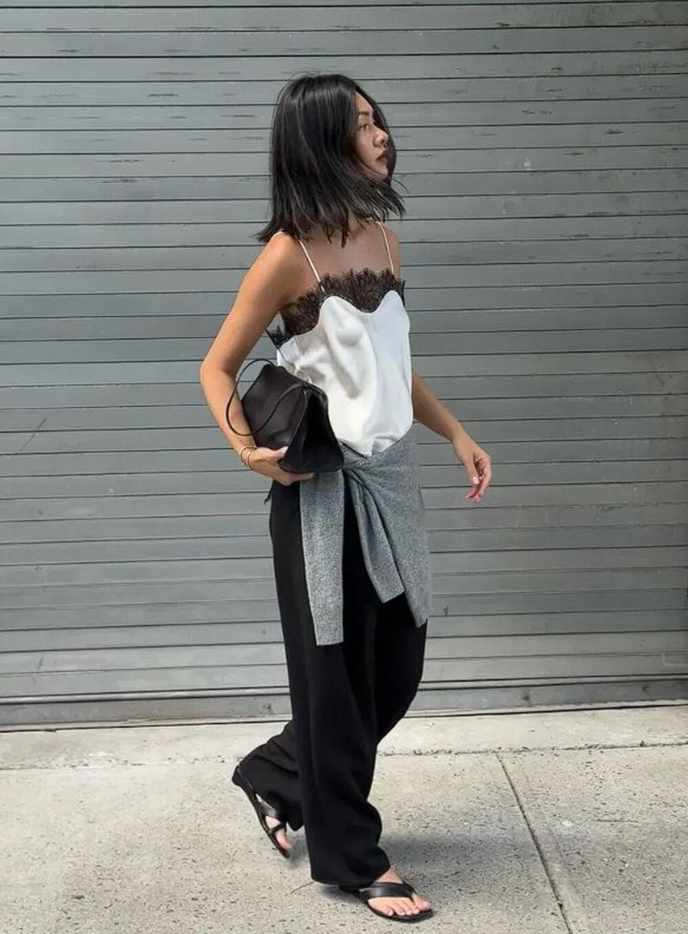 Letnji autfit sastavljen od čipkaste bluze s bretelama, crnih pantalona i japanki